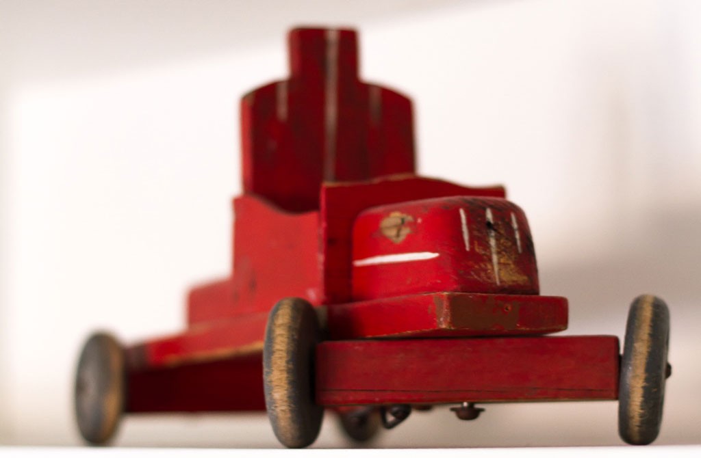 Slitt rød trelekebil med fire hjul på hvit bakgrunn.