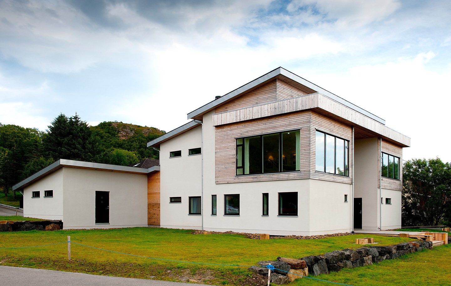 Moderne hvit og trefasade enebolig med store vinduer, grønn plen og trær i bakgrunn