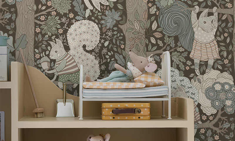 Leketøyseng med stoffmus på stripet dyne, gul koffert og kost foran brunt tapet med ekorn og rådyr