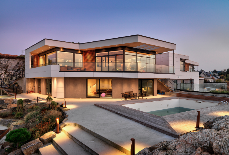 Moderne hvit villa i to etasjer med glassfasade, terrasse og tomt basseng ved skumringshimmel.