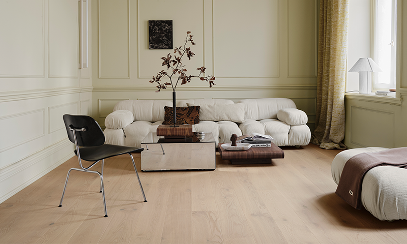 Lyst kremhvit stue med buet sofa, svart stol, lavt glassbord med grener, lyse tregulv