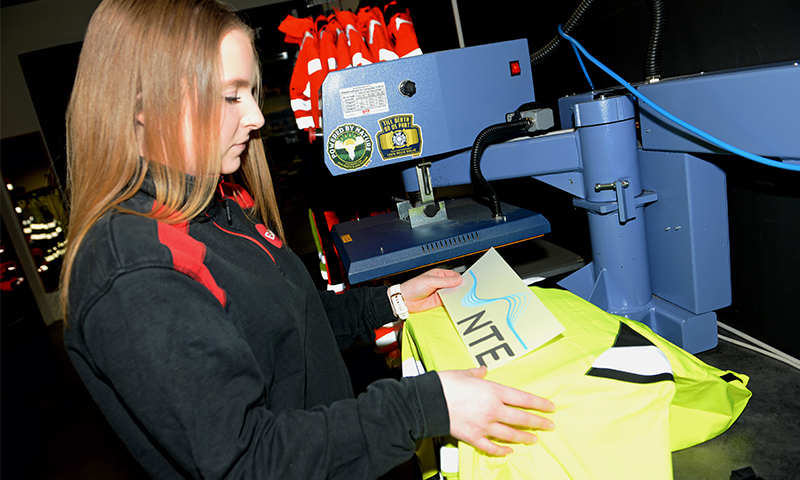 Arbeider ved blå varmepresse overfører NTE-logo på neon gul sikkerhetsjakke