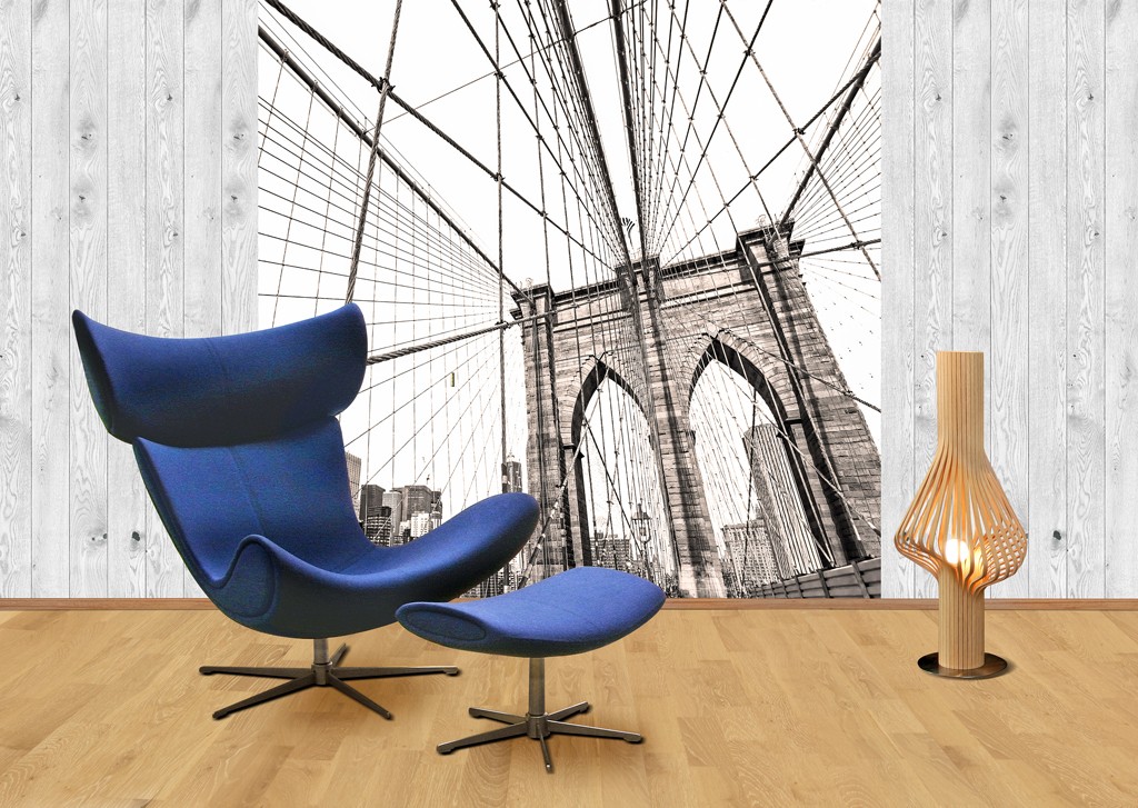 Blå lenestol med fotskammel og lys trelampe foran sort-hvitt bilde av Brooklyn Bridge