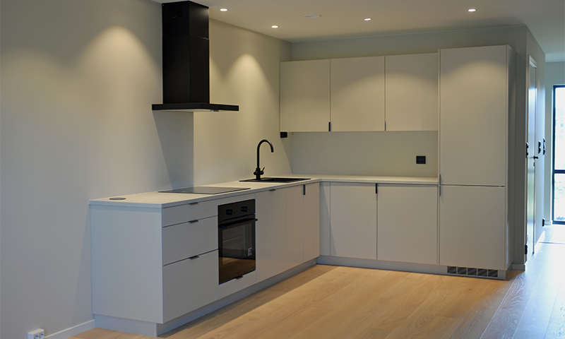 Moderne hvitt kjøkken med L-formede skap, svart ventilator og lys eikeparkett