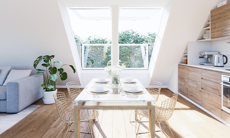 Lyst loftkjøkken med glassbord, fire trådstoler, tregulv, takvindu og grønn utsikt