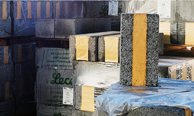 Stablede grå betongblokker med gule striper, pakket i plast i lagerhall