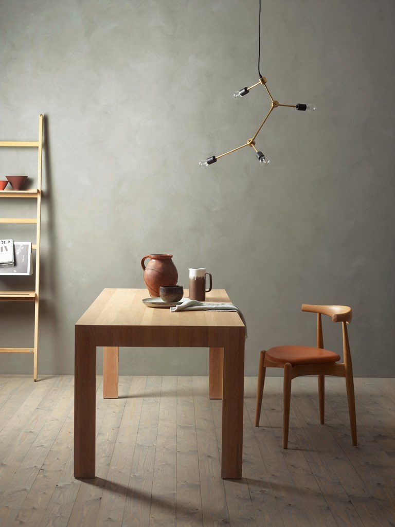 Minimalistisk rom: lyst trebord med keramikkkanne, trestol i skinn og gulllampe