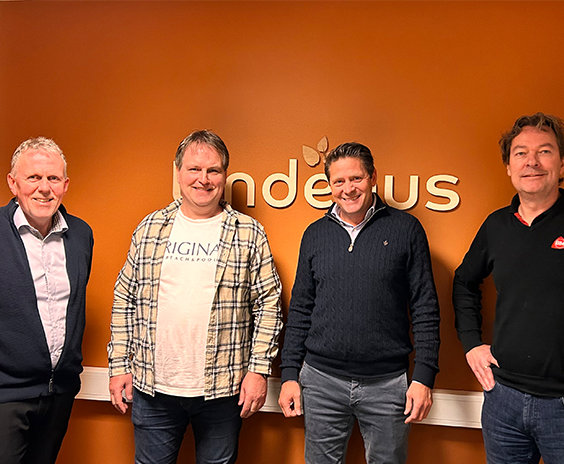 Fire menn i smart-casual står foran oransje vegg med gyllen Indeus-logo og bladmotiv.