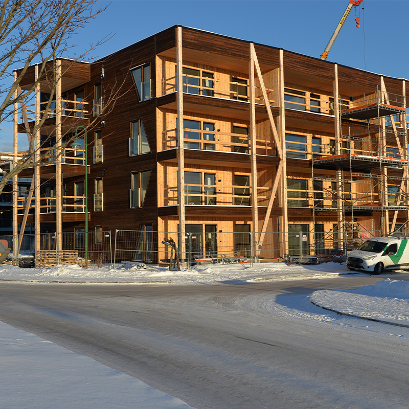 Trebygning under bygging med balkonger, stillas, hvit varebil og blå himmel over snø