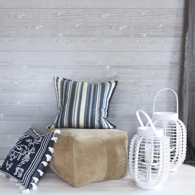 Beige puff med blå-hvit stripete og svart-hvit mønstret pute, to hvite lanterner foran grå vegg