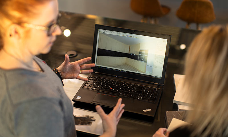 To personer ved bord med åpen laptop som viser 3D-kjøkkendesign i lyse og mørke toner