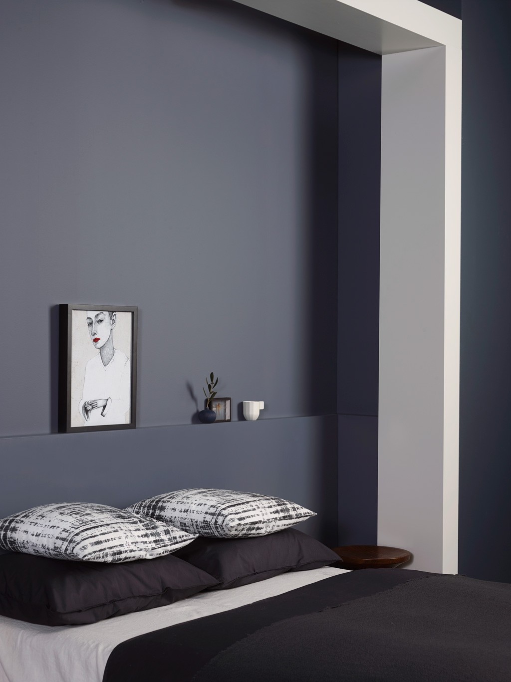 Soverom med mørkeblå vegg og nisje, vase, kopp og skisse bak seng med svarte-hvite puter.