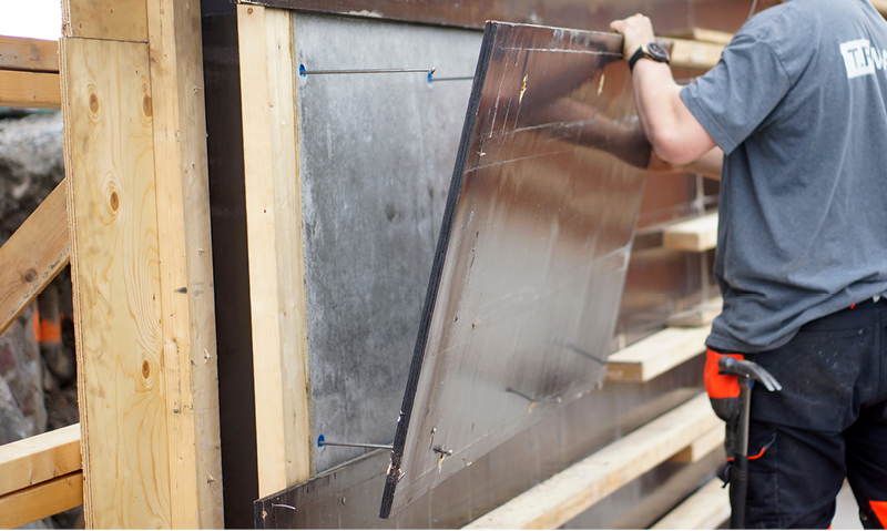 Arbeider fester blankt metallpanel til treramme med blå skruer på byggeplass