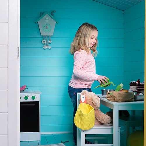 Lekehytte med turkise panelvegger, barn i rosa genser leker ved hvitt kjøkkenbord.