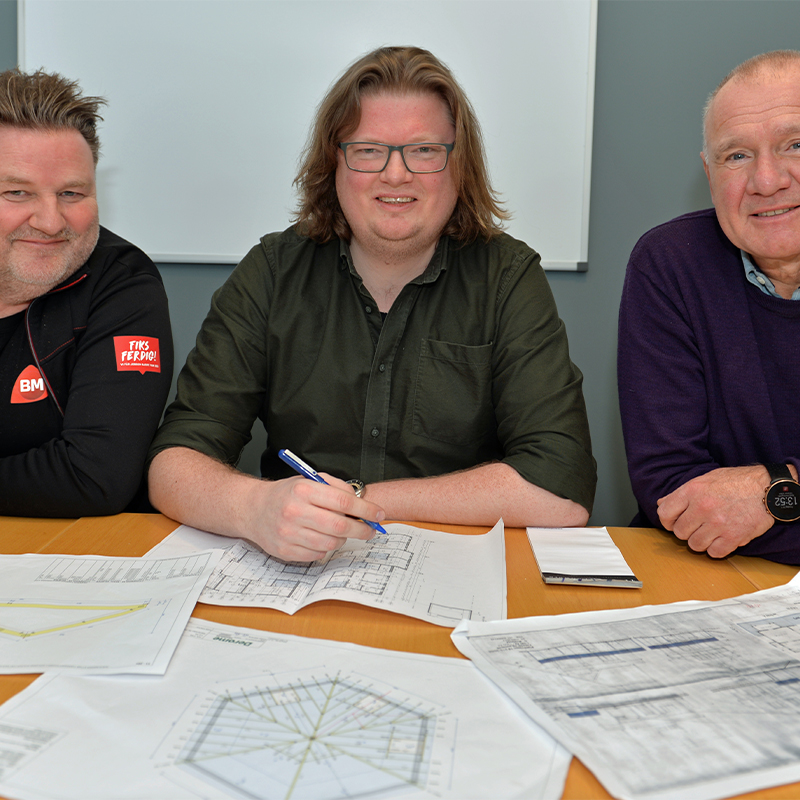 Tre personer ved møtebord med byggetegninger på trebord, én med blå penn.