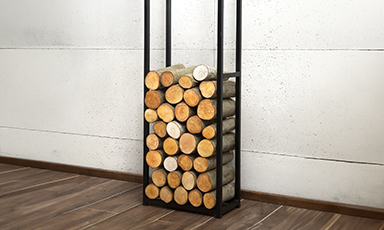 Svart metallstativ med stablet vedkubber foran hvit vegg og tregulv.