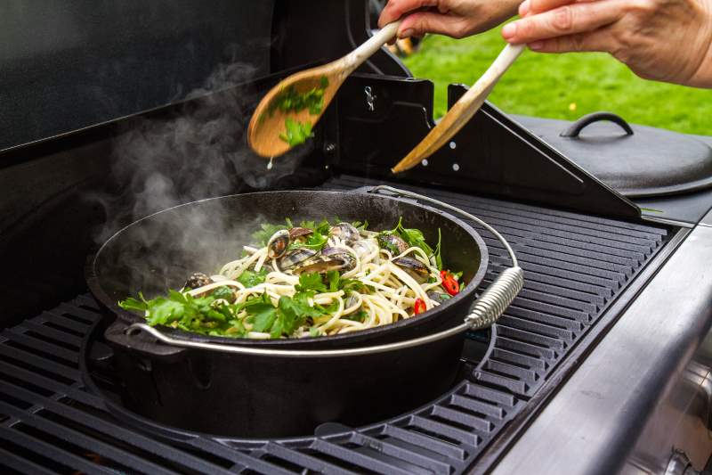 Dampende pasta med blåskjell, chili og persille i svart grillgryte, omrøres med tresleiver