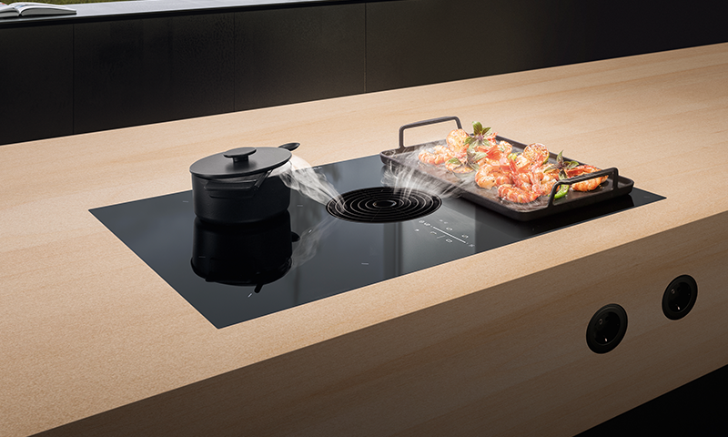Lys kjøkkenøy med svart induksjonsfelt, dampende gryte til venstre og brett med scampi til høyre.