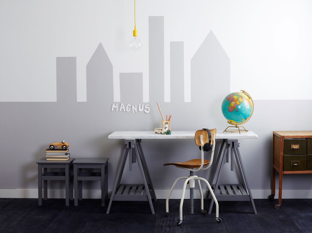 Hvit-grå barnearbeidsplass med bysilhuett, globus, lekebil, penner og skiltet «Magnus»