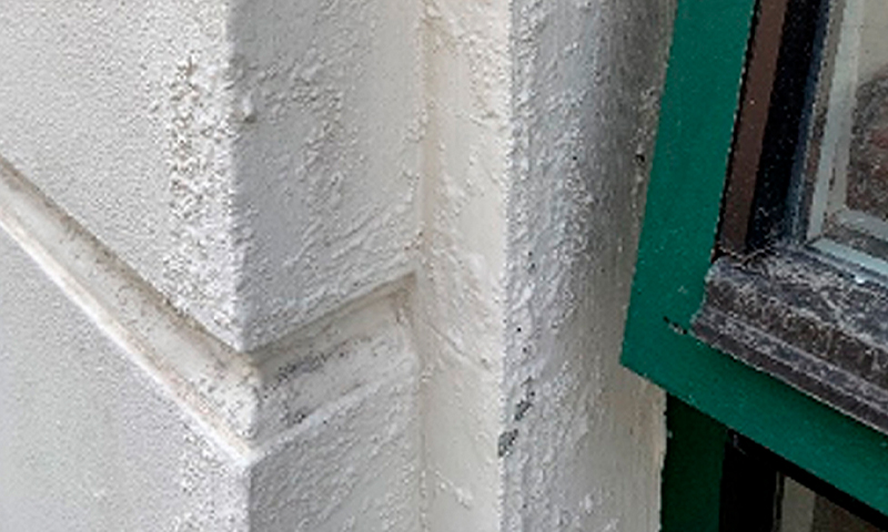 Nærbilde av hjørne mellom hvit pusset fasade og grønn vindusramme.