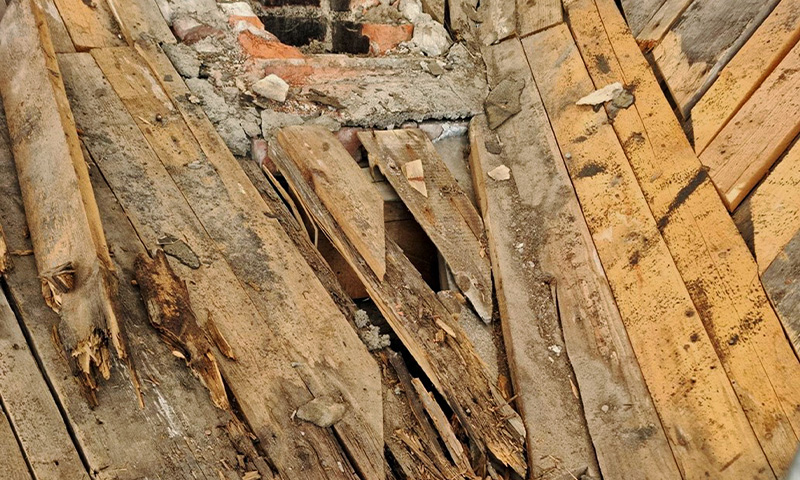 Råtne, ujevne gulvbord av grått og brunt tre med synlig mur under