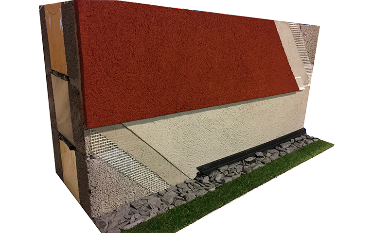 Tverrsnitt av vegg med rød og hvit puss, isolasjon, trestendere, grus og gress.