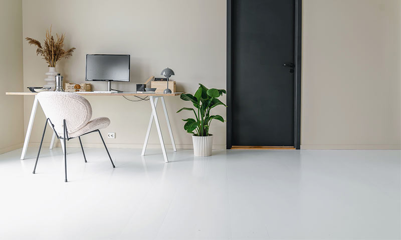 Minimalt hjemmekontor med lyst skrivebord, svart skjerm, kremstol og grønn plante ved svart dør