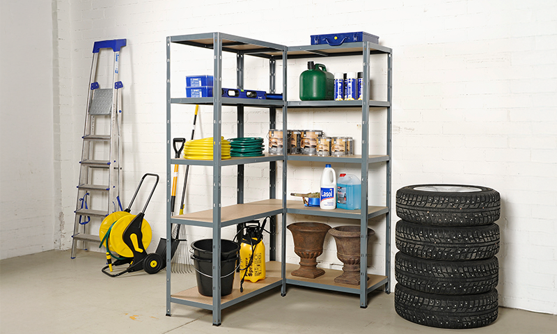 Grå hylle med hageredskaper, gul slange, grønne kanner, rengjøringsmidler og dekk foran hvit vegg