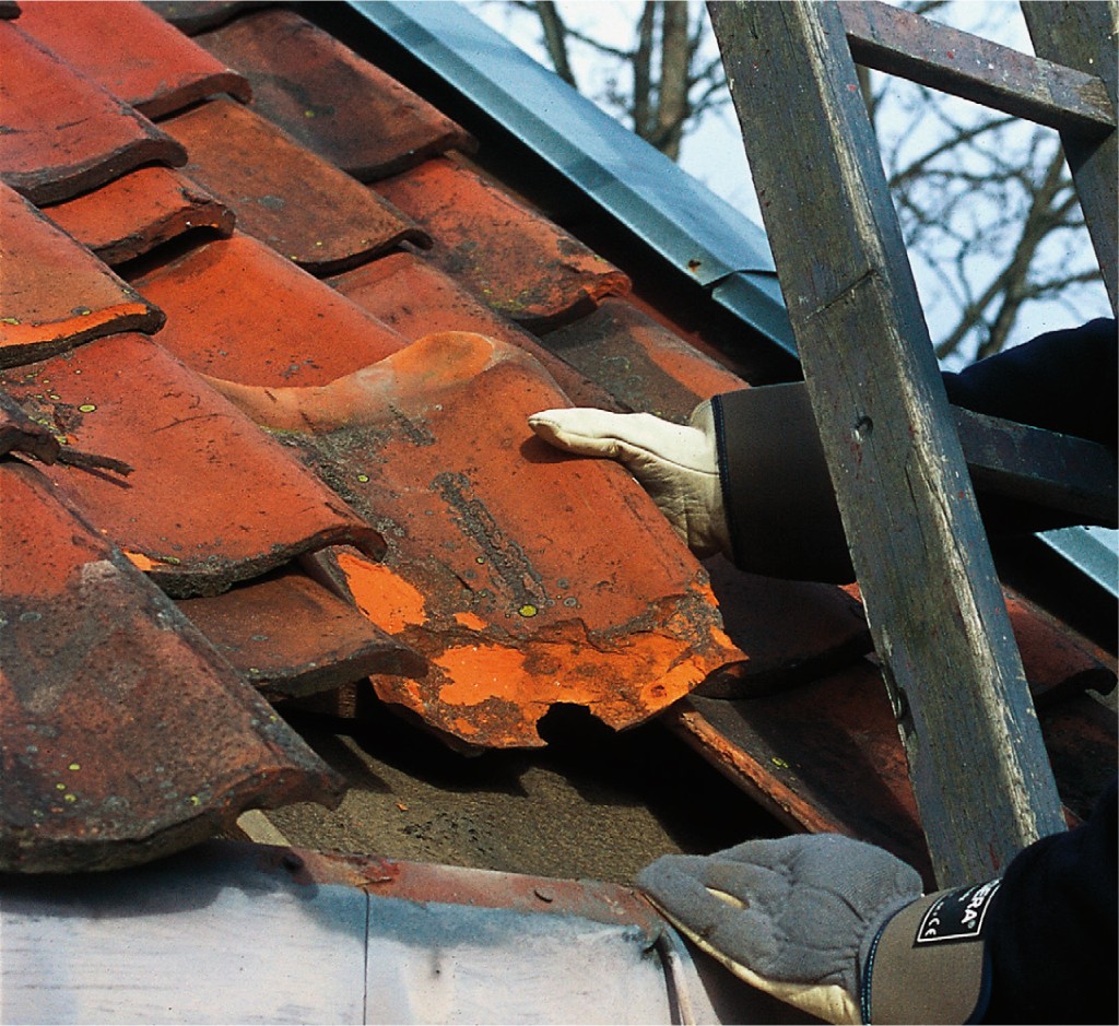 Hvite hansker på stige fjerner sprukket, flasset rød takstein