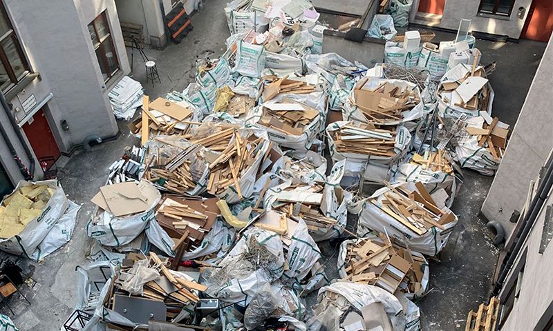 Hvite bagger med bygningsavfall (tre, papp, isolasjon) stablet i gårdsrom