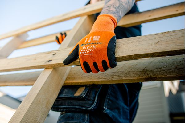 Nærbilde av tatovert arm med oransje arbeidshanske som griper en trestige.