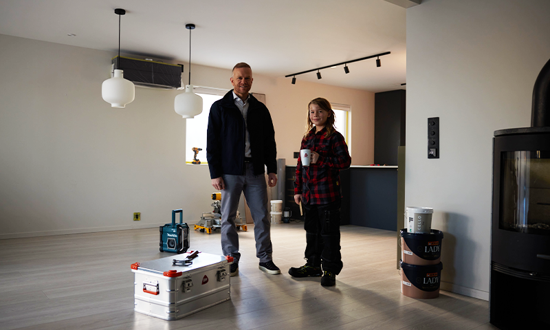 To personer i moderne stue under oppussing med lyse parkett, verktøy og hvit kaffekopp.