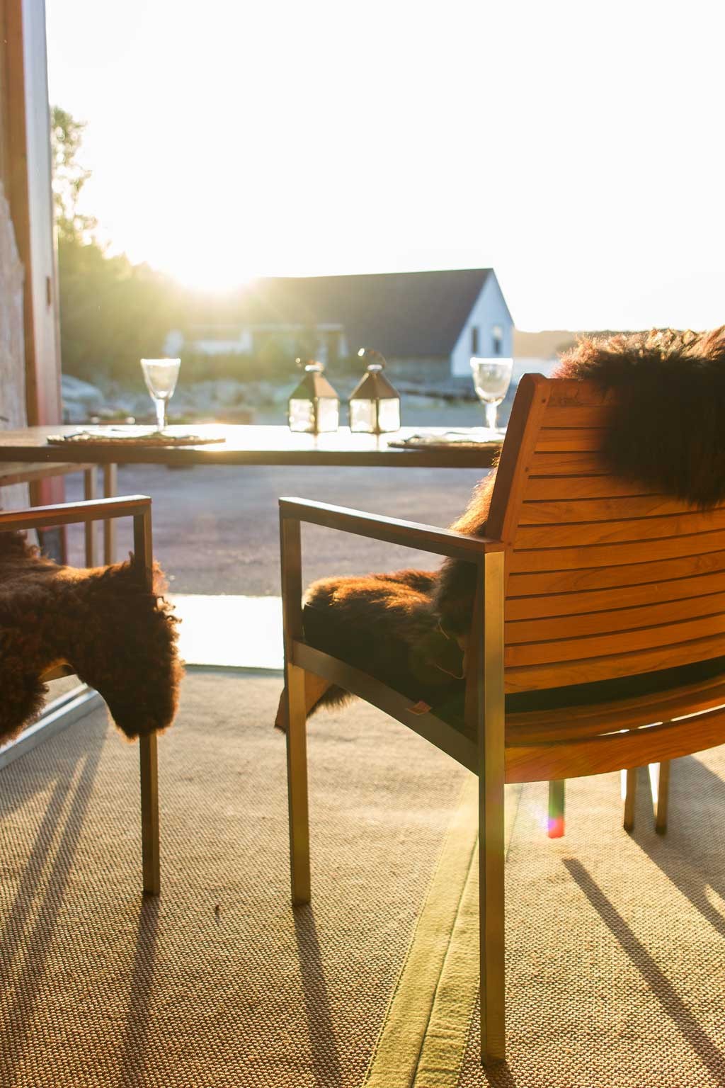 To trebordstoler med brun saueskinn, trebord med lykter og vinglass i gyllent sollys