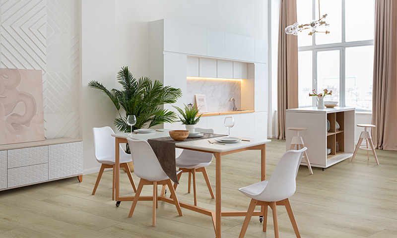 Lyst, moderne kjøkken- og spiseområde med hvite møbler, trebord, innendørsplanter og stort vindu