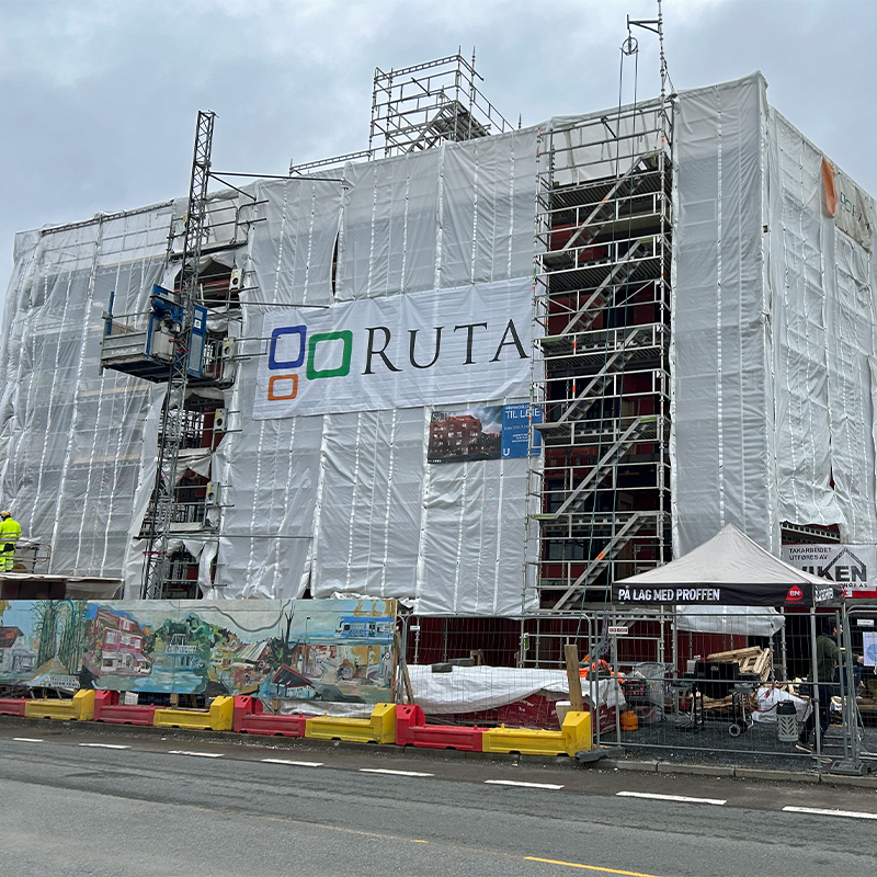 Stillasdekket bygg innpakket i hvit presenning med Ruta-banner, gule og røde sperringer.