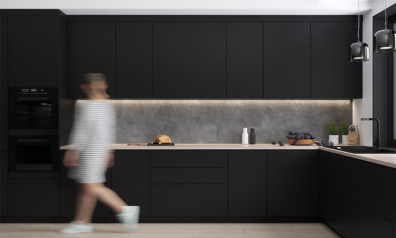 Moderne svart kjøkken med eikebenk, lys under skap, brød, fruktfat og sløret person