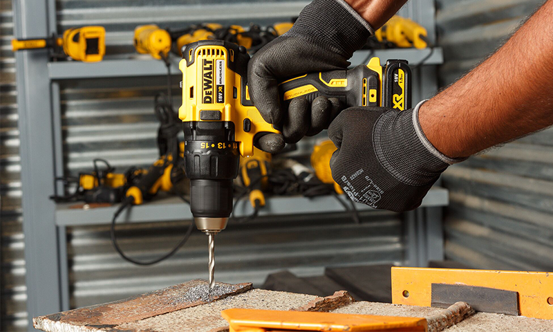 Nærbilde: person i svarte hansker bruker gul-svart DeWalt-bormaskin på rustent metall i verksted
