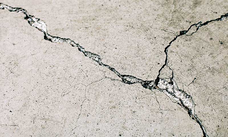 Nærbilde av lys grå betonggulv med en mørk, krokete sprekk.