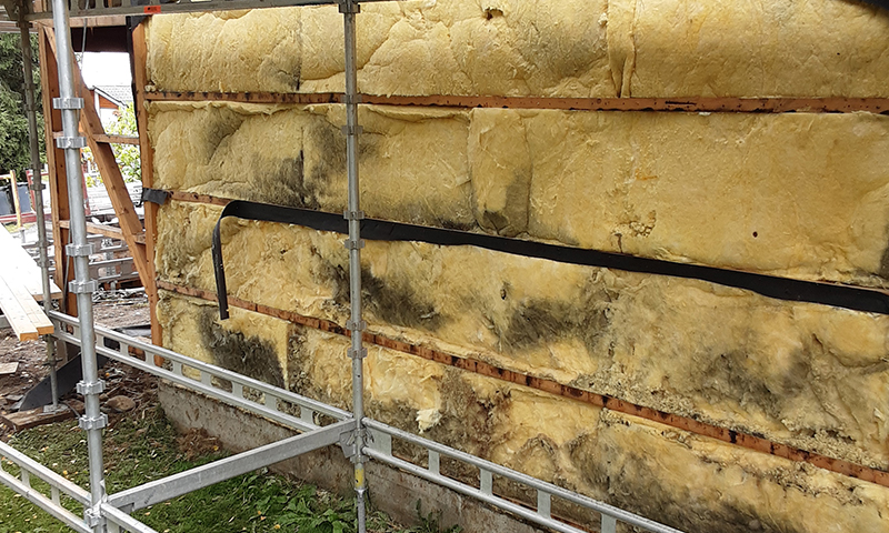 Metallstillas foran husfasade med gul isolasjon og mørke muggflekker