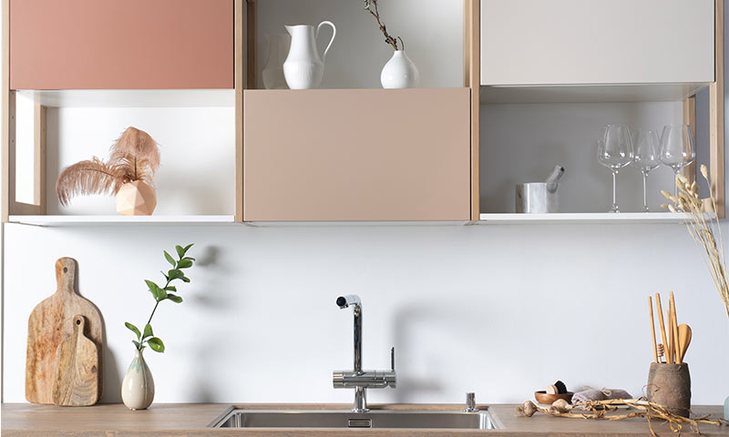 Minimalistisk kjøkken med lyserosa og beige skap, stålkran, vaser, skjærefjøler og vinglass