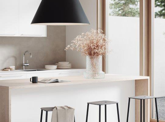 Lyst kjøkken med hvit øy i tre, svart pendellampe, tre svarte krakker og vase med tørkede blomster.