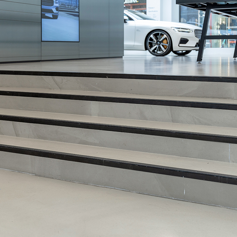 Grå trapp med svarte kanter foran hvit luksussedan i moderne bilutstilling.