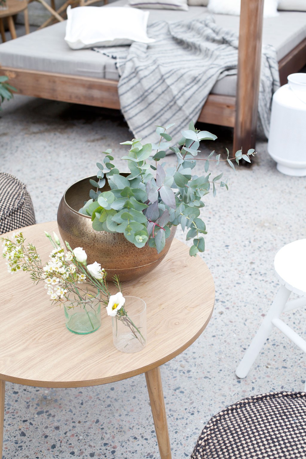 Trebord med bronsebolle fylt av eukalyptus, to glassvaser med hvite blomster på grått gulv.