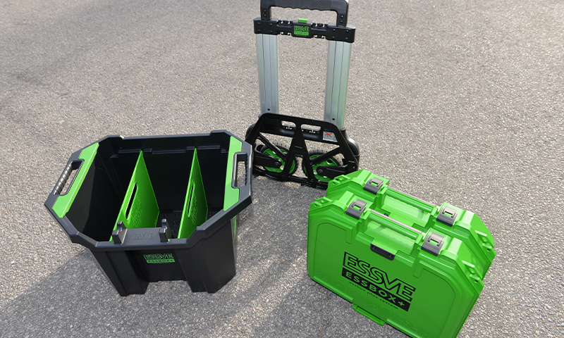 Tre grønne og svarte verktøykasser på grå asfalt: åpen boks, sammenleggbar trille og lukket koffert.