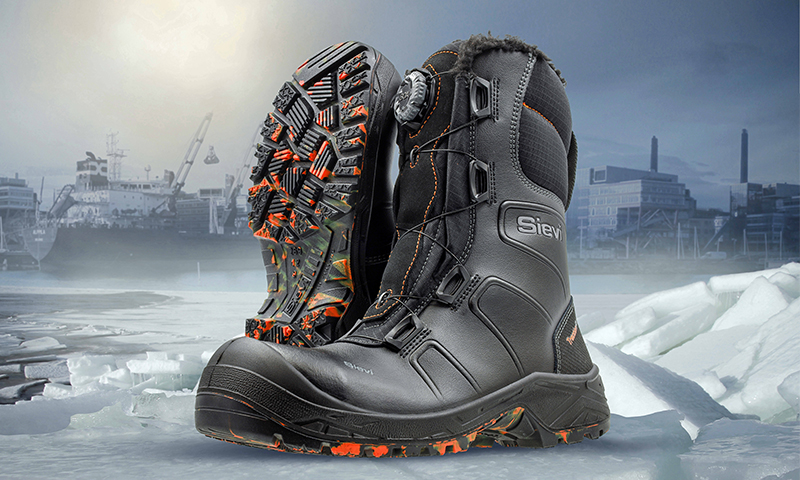 Svart par vinterarbeidsstøvler med oransje såle, plassert på is ved industrihavn