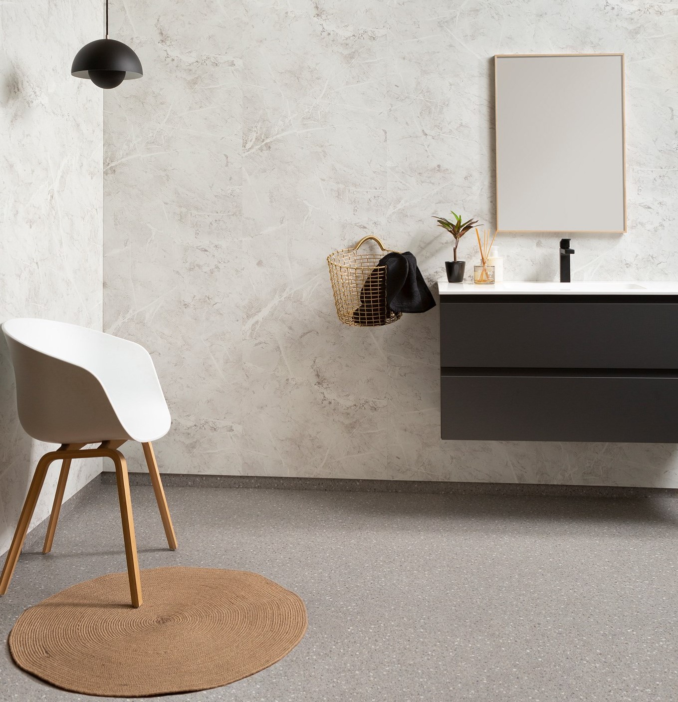 Minimalistisk baderom med hvit stol, rund brun matte, svart servant, gullkurv og grønn plante.