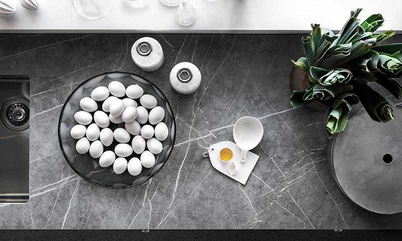 Grå marmorbenk med bolle full av hvite egg, små krukker, knust egg i målekopp og grønn plante.