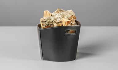 Svart lærkurv fylt med bjørkved på grå bord- og bakgrunn.