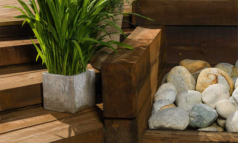Ute: grønn plante i grå betongkrukke på brun treterrasse ved lyse dekorsteiner.
