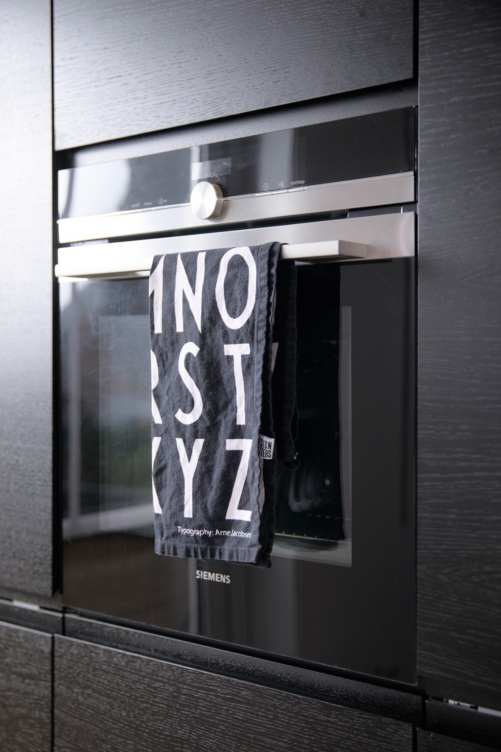 Moderne svart Siemens-ovn i mørkt kjøkkenskap med svart-hvitt kjøkkenhåndkle i håndtak.